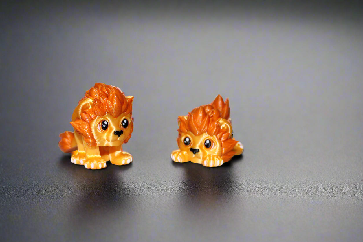 Two toy lion figures on a white surface with green leaves in the background