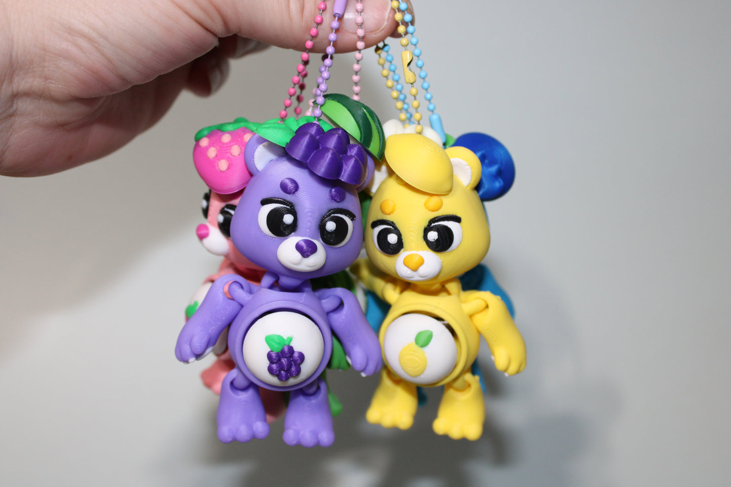 Colorful toy figures on keychains held by a hand against a plain background